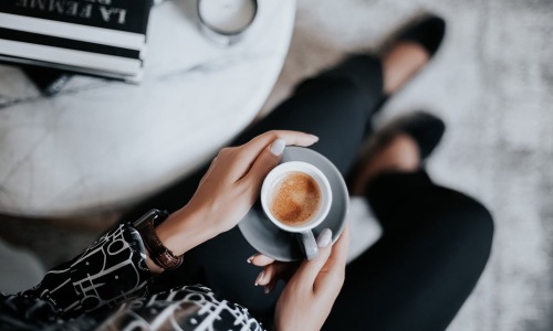 business woman sits next to a marble table with books and holds a saucer with a cup of espresso